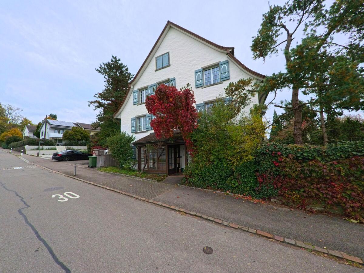 In einer Tempo-30-Zone von Matzingen (9548, Kanton Thurgau) steht ein grosses Haus mit hellblauen Fensterläden, umgeben von dichtem Grün und rotem Herbstlaub.