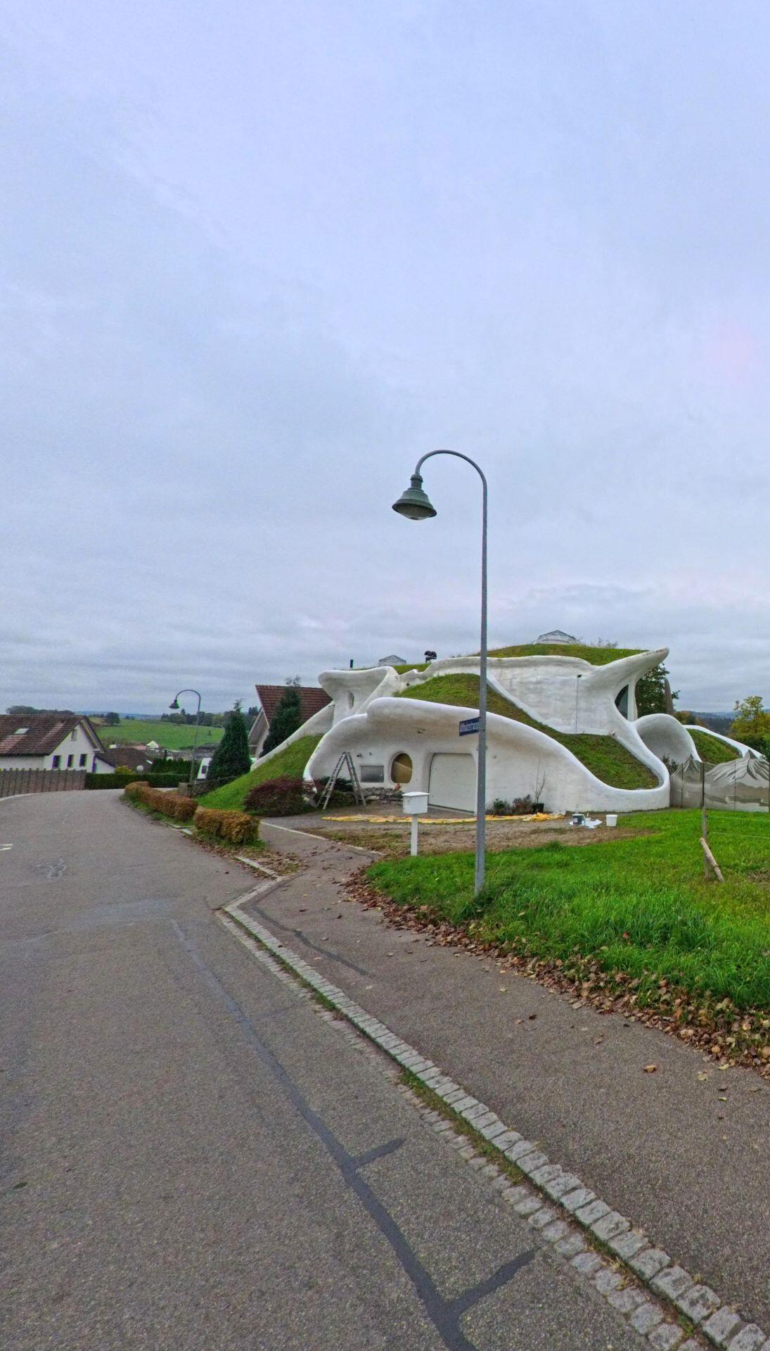 Am Hang in Matzingen (9548, Kanton Thurgau) fällt ein organisch geformtes, weiss verputztes Gebäude mit begrüntem Dach neben der Strasse auf.