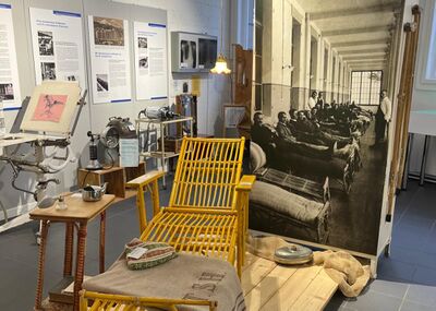 Im Medizinmuseum Davos in Davos Platz (7270, Kanton Graubünden) zeigt eine Ausstellung historische medizinische Geräte, ein gelbes Liegebett und ein grosses Foto von Patienten in einer Sanatoriumshalle.