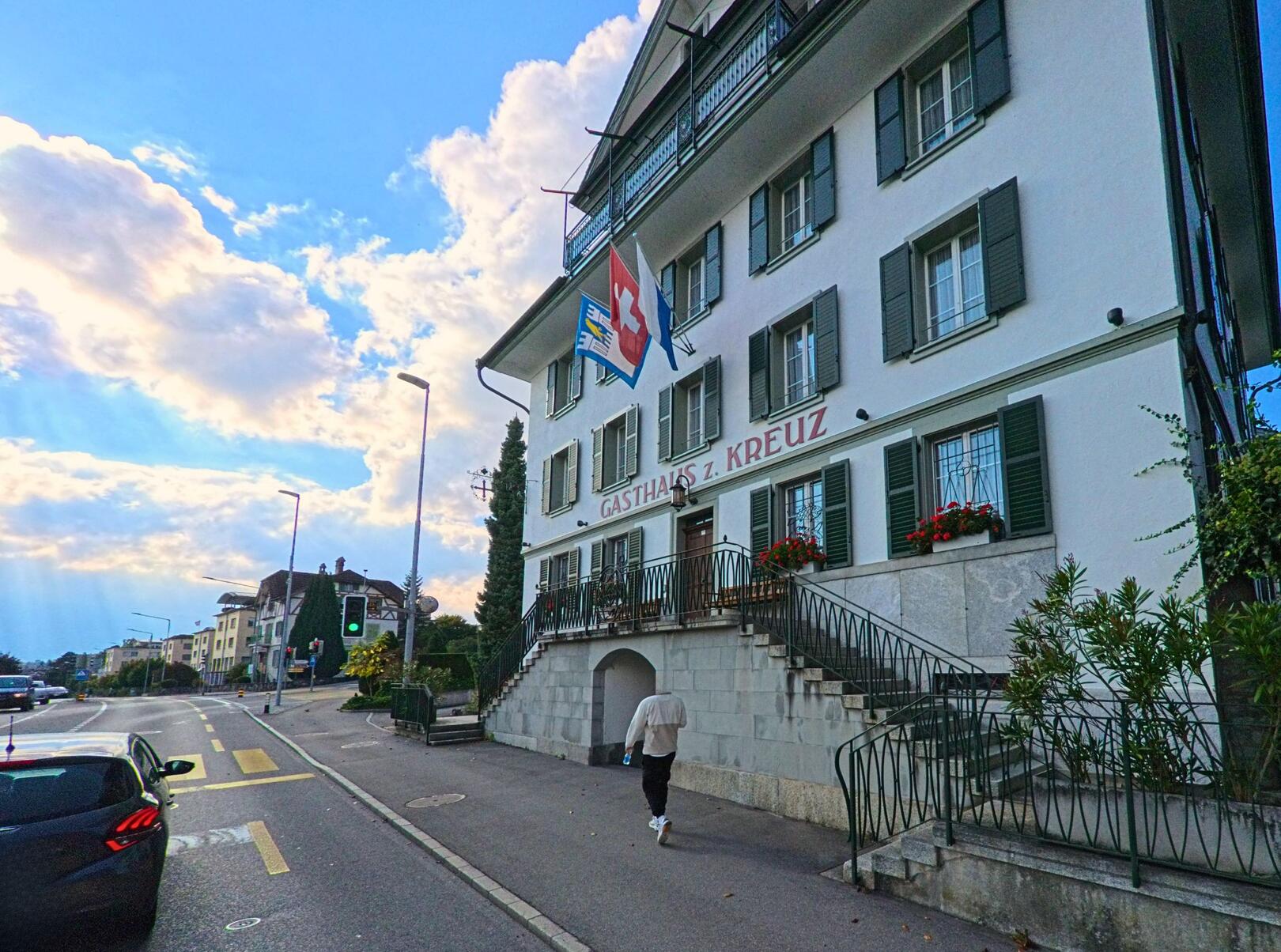 Das Gasthaus zum Kreuz in Meggen (6045, Kanton Luzern) ist ein markantes Gebäude mit einer auffälligen Fassade und zwei Fahnen, das eine einladende Atmosphäre vermittelt.