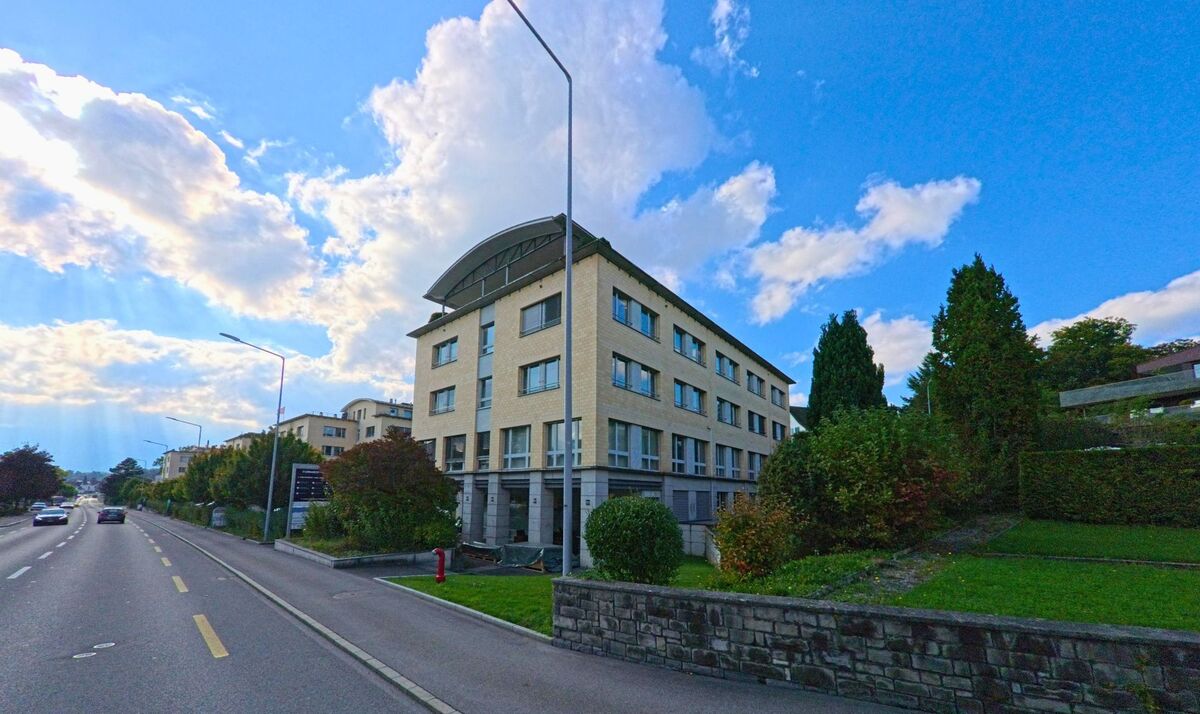 Ein mehrstöckiges Wohngebäude steht an einer leicht ansteigenden Strasse in Meggen (6045, Kanton Luzern).