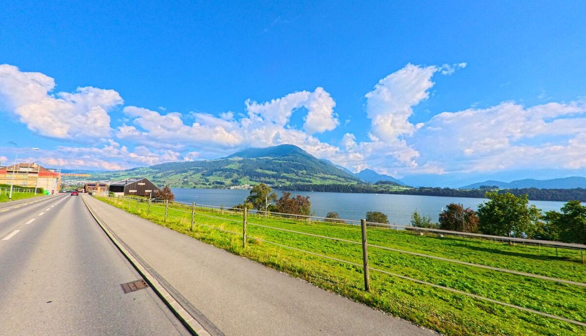 Entlang einer Strasse eröffnet sich der Blick auf den See und die Landschaft bei Meggen (6045, Kanton Luzern).