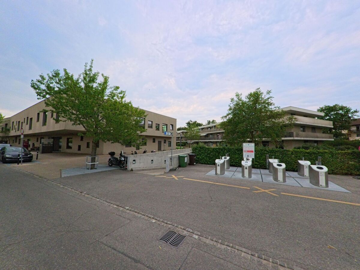 In Meinier (1252, Kanton Genf) befindet sich eine Recyclingstation vor modernen Wohnhaeusern mit grossen Balkonen.