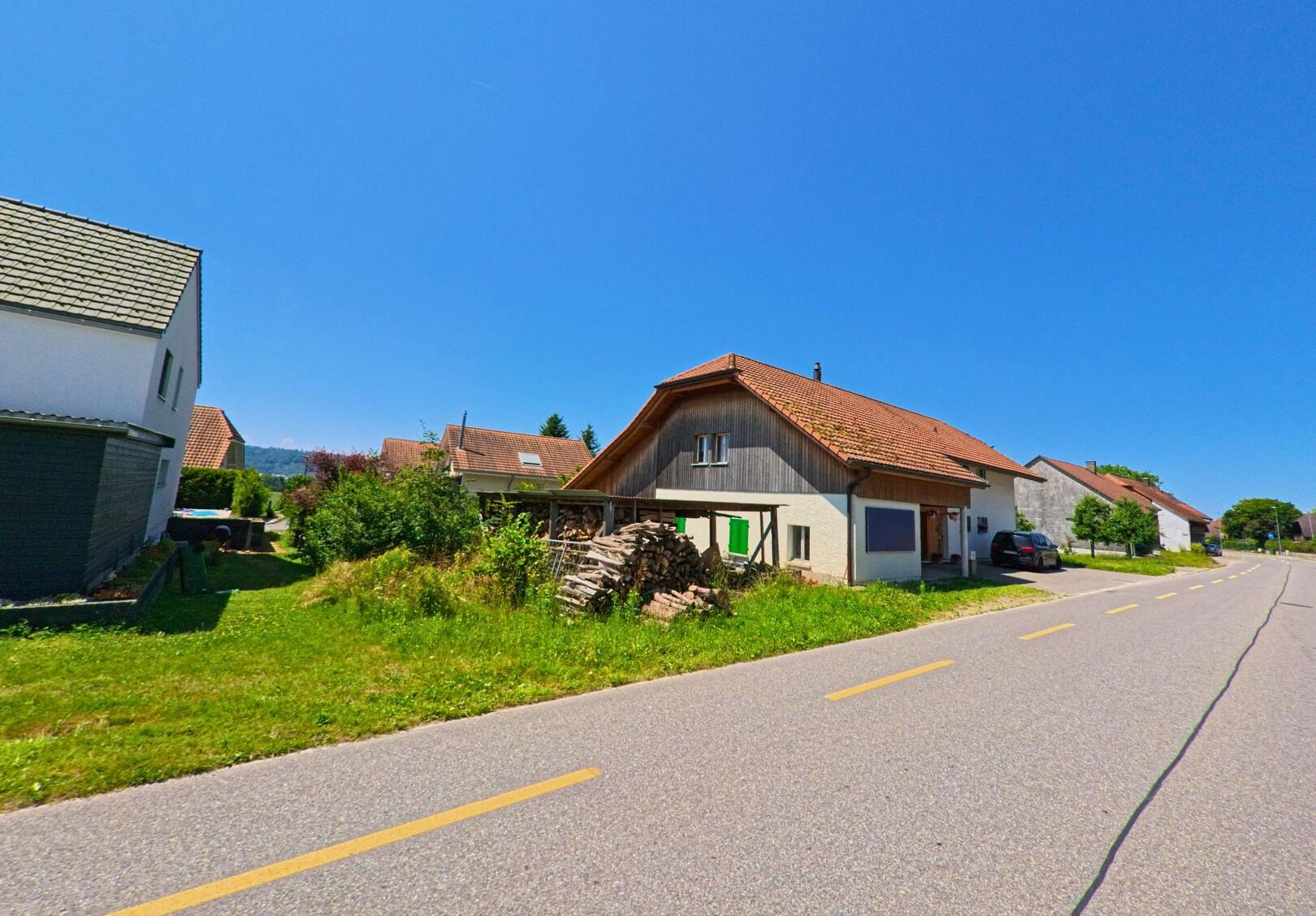 Entlang der Hauptstrasse in Meinisberg (2554, Kanton Bern) stehen Wohnhäuser mit Satteldächern, vor denen Brennholz gestapelt ist.
