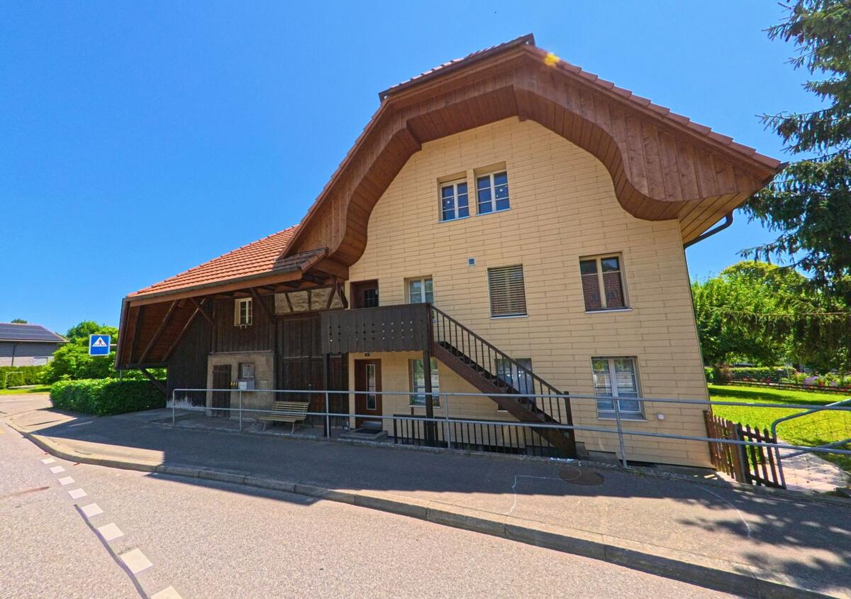 In Meinisberg (2554, Kanton Bern) steht ein traditionelles Wohnhaus mit geschwungenem Walmdach und hölzerner Aussentreppe an einer leicht abschüssigen Strasse.