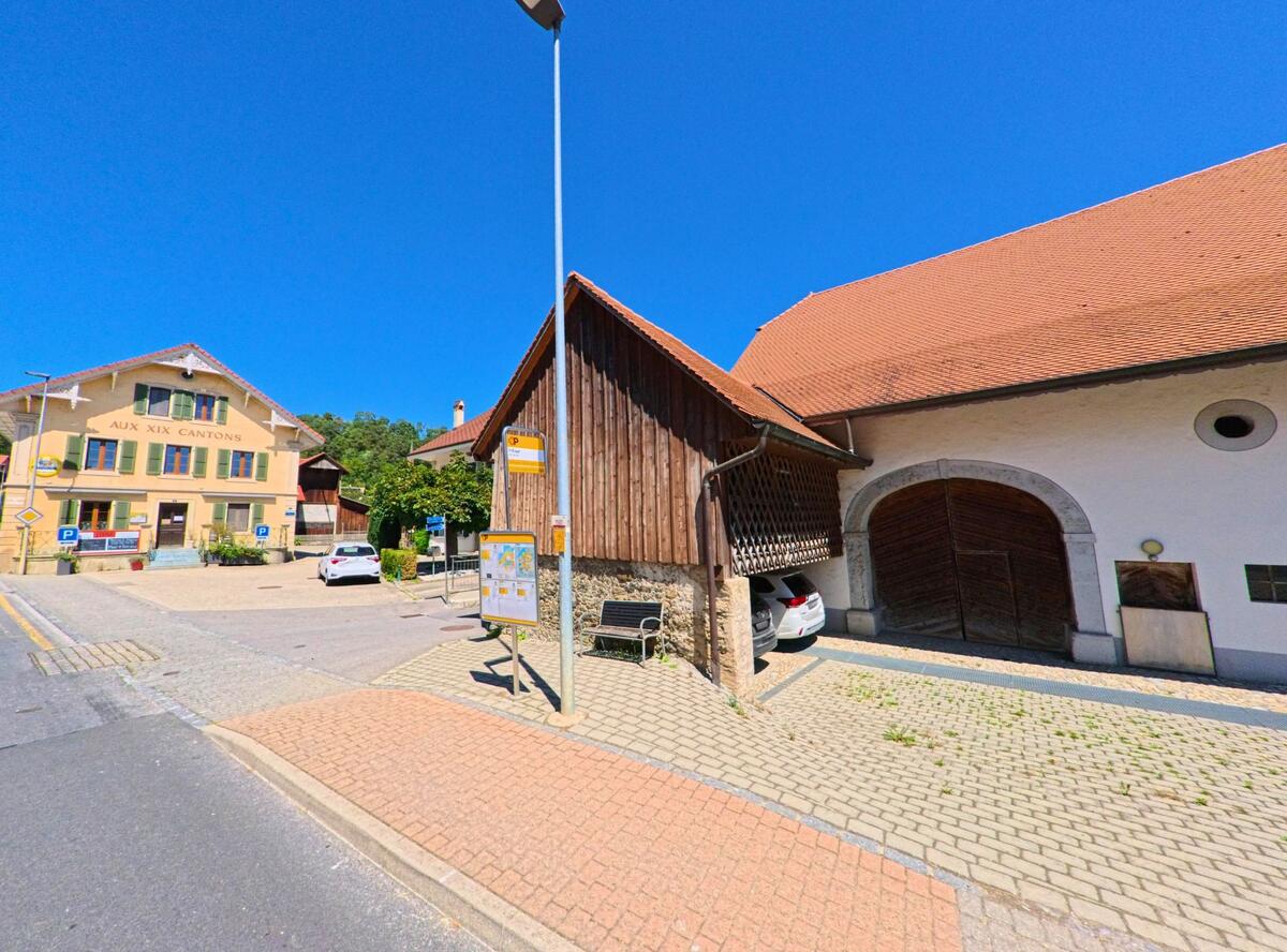 Im Zentrum von Ménières (1533, Kanton Freiburg) befindet sich eine Bushaltestelle vor einem traditionellen Gasthaus und einer grossen Scheune.