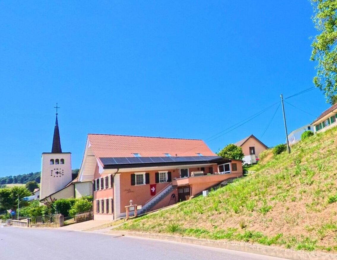 Blick auf das Dorfzentrum von 1533 Ménières (FR) mit Kirche, Wohnhäusern und der ruhigen, ländlichen Umgebung.