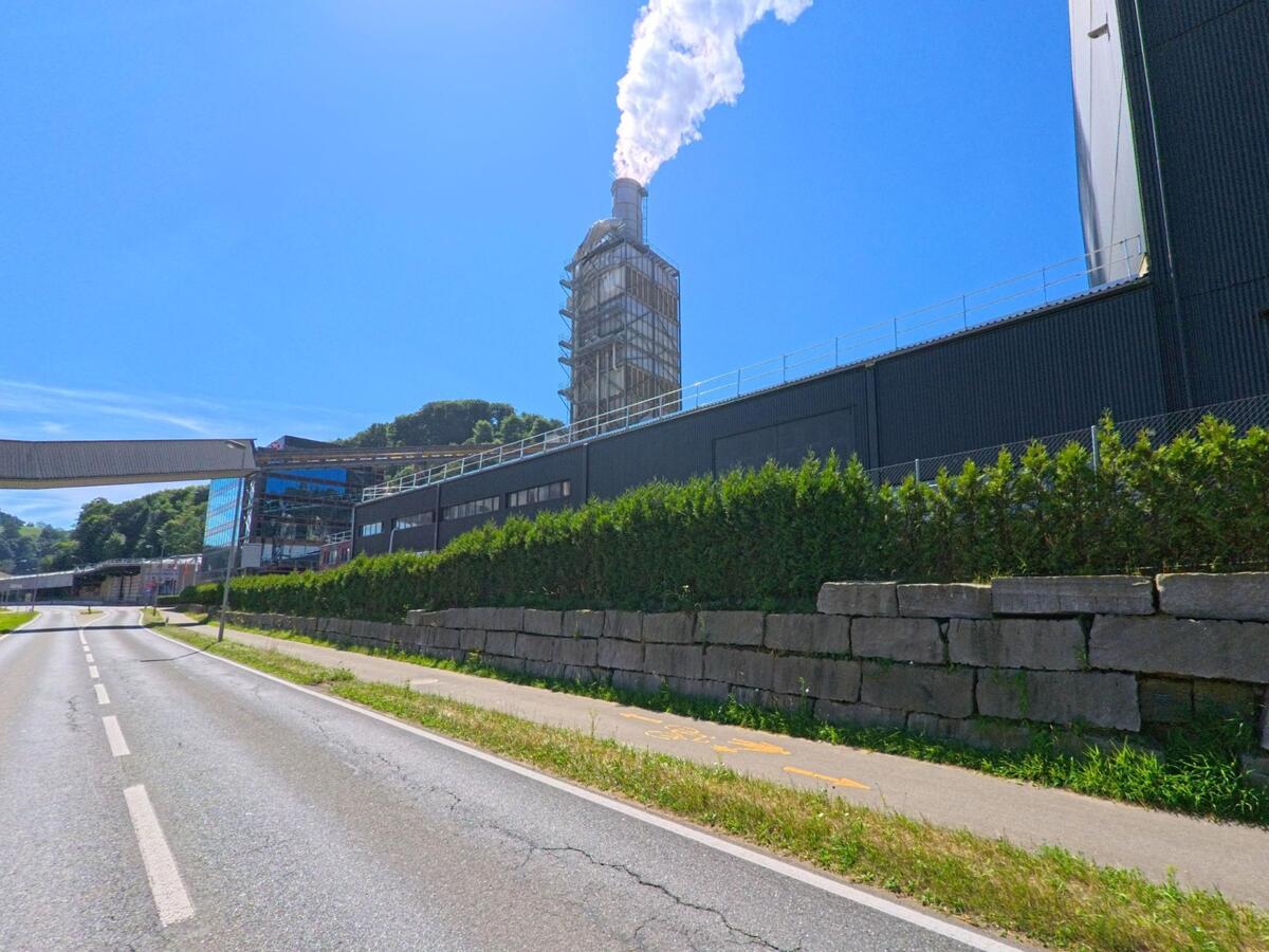 In Menznau (6122, Kanton Luzern) verläuft eine Strasse an einem grossen Industriekomplex entlang, aus dessen Schornstein weisse Dampfwolken aufsteigen.