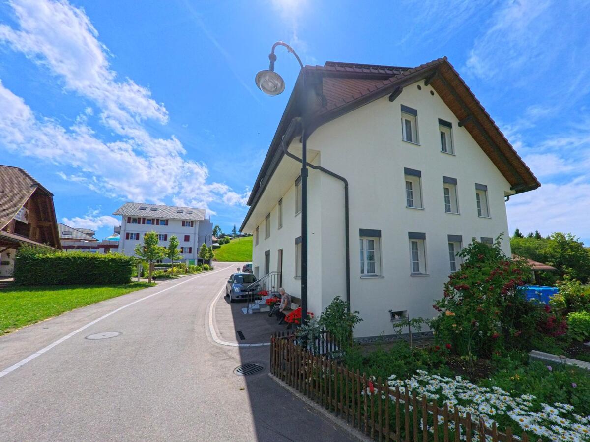 Ein Wohnhaus mit gepflegtem Vorgarten steht in Menznau (6125, Kanton Luzern) an einer schmalen Quartierstrasse, die sich durch die leichte Hügellandschaft zieht.