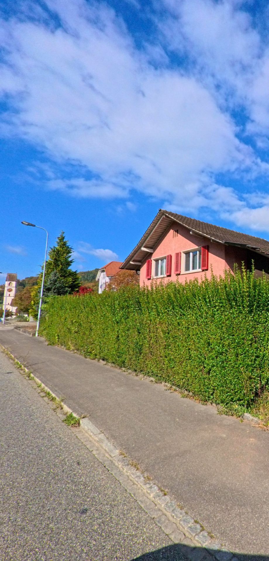 Ein grosses Wohnhaus mit gruener Fensterlaeden steht in Mettauertal (5273, Kanton Aargau) an einer leicht gekruemmten Strasse mit Blick auf die umliegenden Huegel.