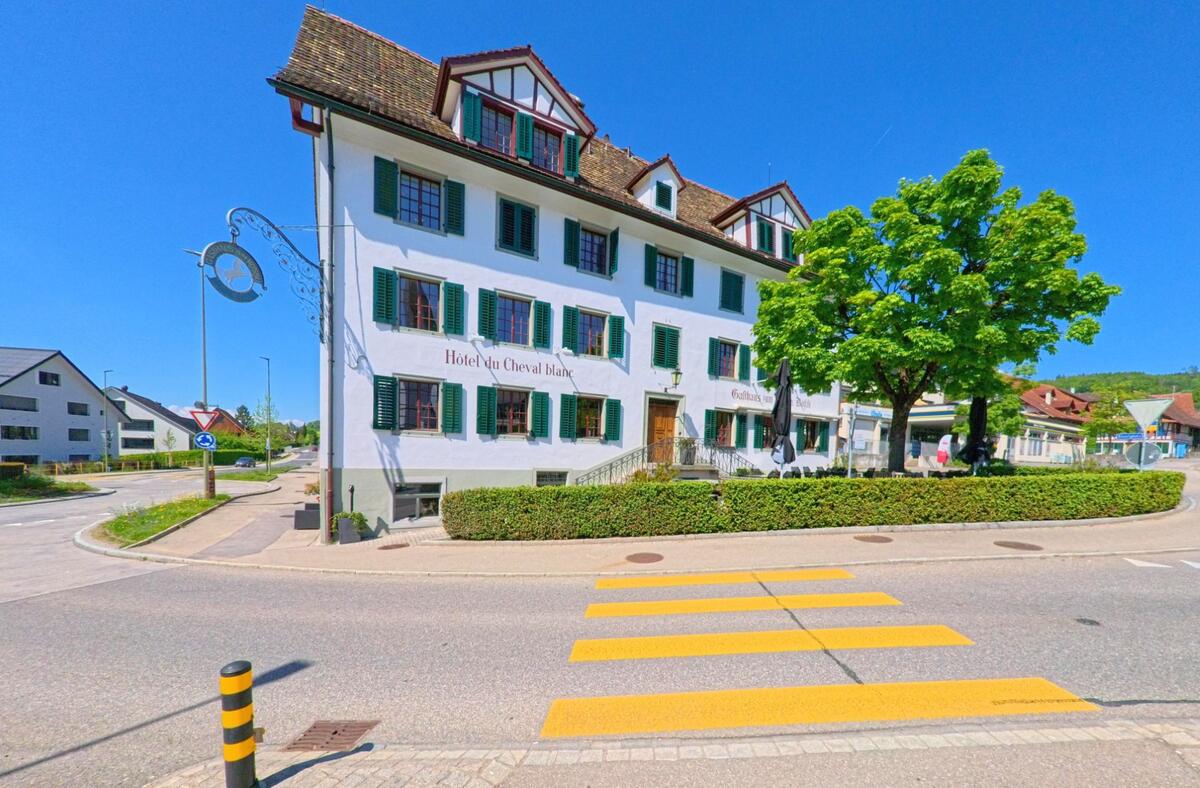 An der Hauptstrasse in Mettmenstetten, PLZ 8932 im Kanton Zürich steht das traditionsreiche Gebäude des Hôtel du Cheval blanc mit grünen Fensterläden und Gasthausterrasse.