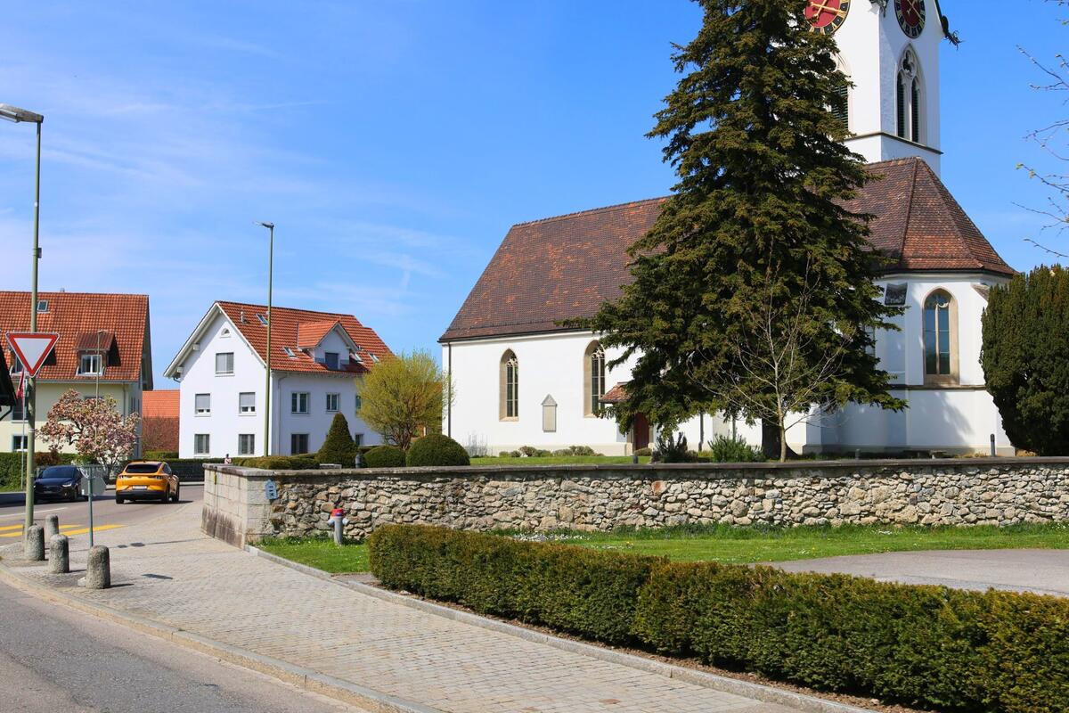 Die reformierte Kirche mit ihrem markanten Uhrturm steht in Mettmenstetten, PLZ 8932 im Kanton Zürich hinter einer historischen Natursteinmauer an einem kleinen Platz.