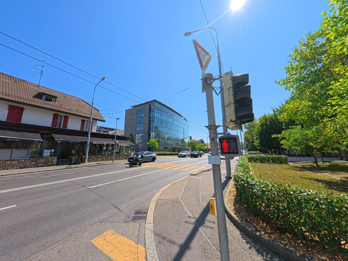 An einer Hauptstrasse in Meyrin (1216, Kanton Genf) zeigt die Ampel rotes Signal, waehrend gegenueber moderne und traditionelle Gebaeude nebeneinander stehen.