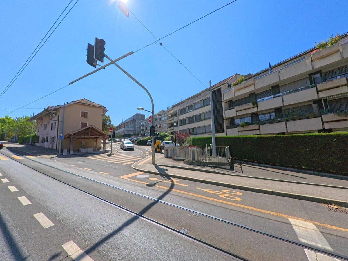 In Meyrin (1217, Kanton Genf) verläuft eine Strasse mit Tramgleisen und Ampelanlage an Wohnhaeusern und einem kleinen Gebaeude vorbei.
