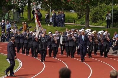 Eine Brass Band marschiert in Rehetobel (9038, Kanton Appenzell Ausserrhoden) in Formation ueber eine Laufbahn und spielt dabei ihre Blasinstrumente.