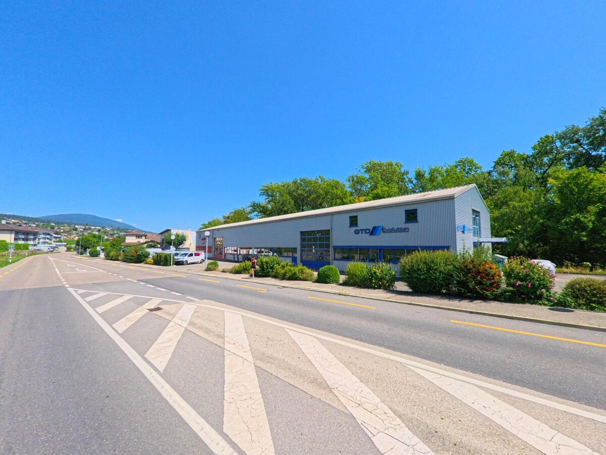 Am Rand einer breiten Strasse in Milvignes (2012, Kanton Neuenburg) steht ein modernes Industriegebaeude mit dem Schriftzug GTO Evolution, umgeben von Bueschen und Baumen.
