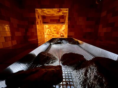 Im Mineralbad und Spa Samedan (7503, Kanton Graubuenden) leuchten warme Farben in einem Raum mit Steinen und Fliesen im sanften Licht.