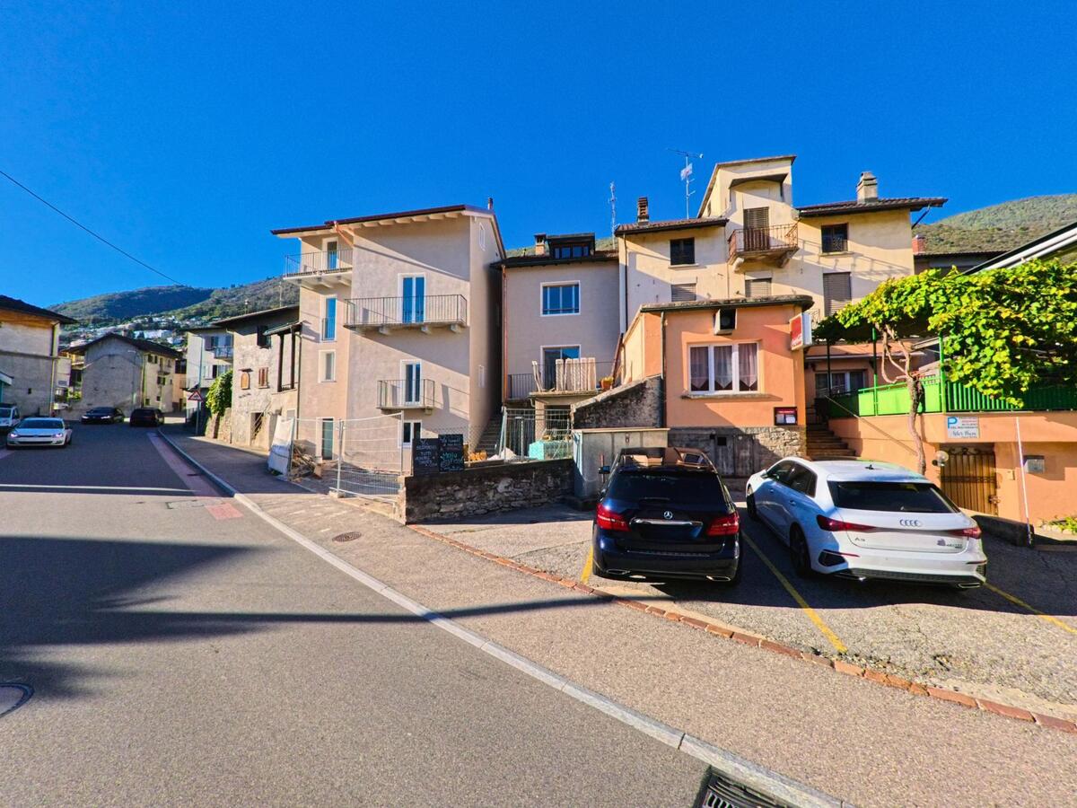 In Minusio (6648, Kanton Tessin) stehen mehrere Wohnhäuser eng beieinander an einer ruhigen Strasse mit geparkten Autos und Blick auf die Hügel.