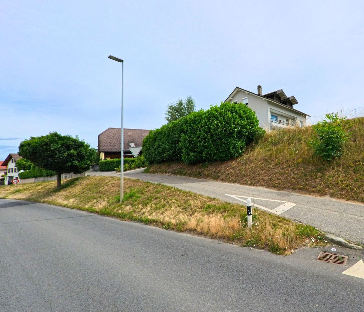 In Misery-Courtion (PLZ 1721, Kanton Freiburg) führt ein schmaler Gehweg eine Böschung hinauf zu einem Wohnquartier mit gepflegten Hecken und Einfamilienhäusern.