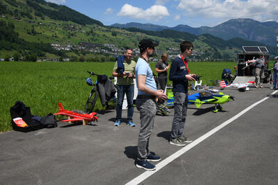 Mehrere Personen steuern Modellflugzeuge auf einer Startflaeche vor Berglandschaft in Oberdorf (6370, Kanton Nidwalden) bei sonnigem Wetter.