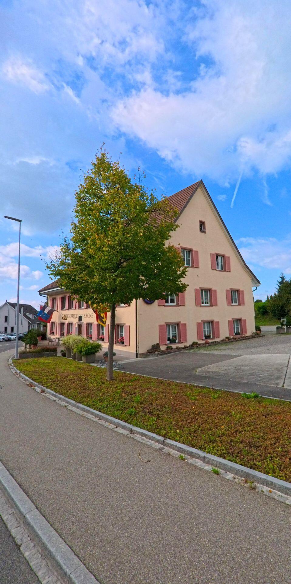 Das Gasthaus Krone in Möhlin (4313, Kanton Aargau) steht an einer gepflasterten Strasse, geschmückt mit Fahnen und umgeben von gepflegten Grünflächen.