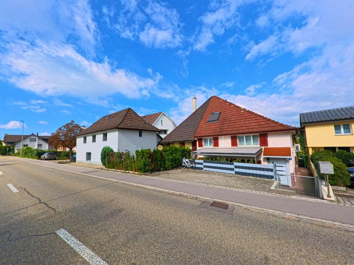Entlang einer Hauptstrasse in Möhlin (4313, Kanton Aargau) reihen sich Einfamilienhäuser mit gepflegten Vorgärten und roten Ziegeldächern.