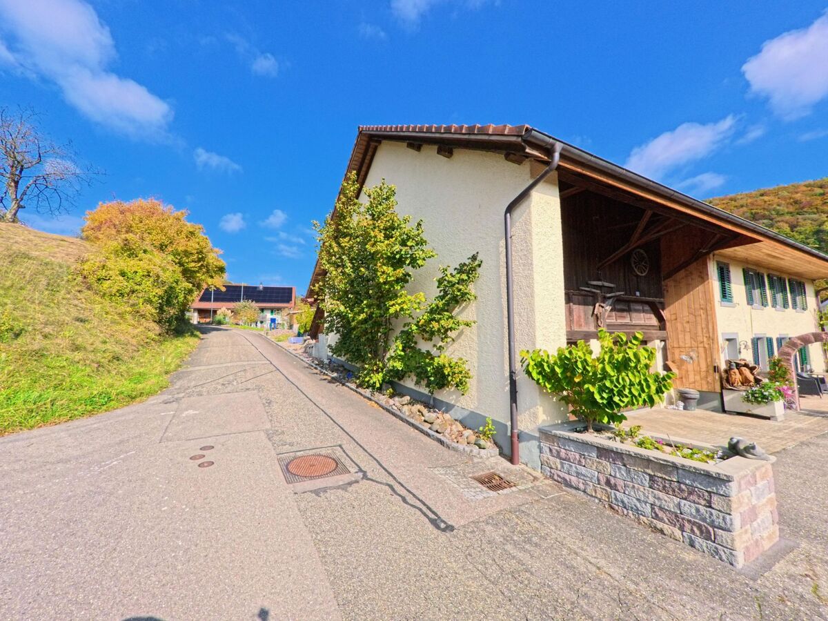 Eine schmale, ansteigende Gasse mit traditionellen Wohnhäusern und begrünten Vorgärten liegt in Mönthal (5237, Kanton Aargau) unter blauem Himmel.