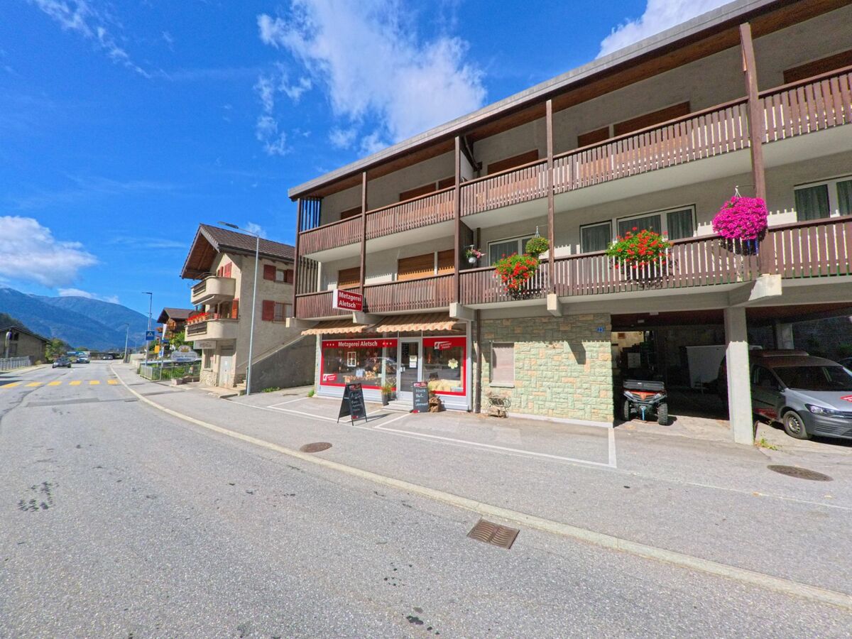 In Mörel-Filet (3983, Kanton Wallis) befindet sich eine Metzgerei mit roten Markisen in einem Gebäude mit Holzbalkonen und Blumenschmuck.