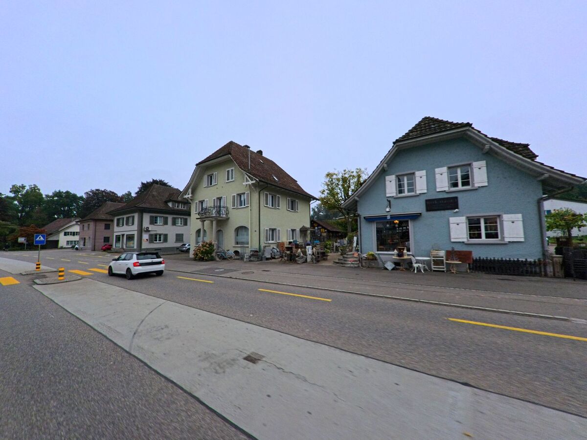 Entlang der Hauptstrasse in Möriken-Wildegg (5103, Kanton Aargau) stehen gepflegte Wohnhäuser und ein kleines Geschäft mit dekorativen Aussenbereichen.
