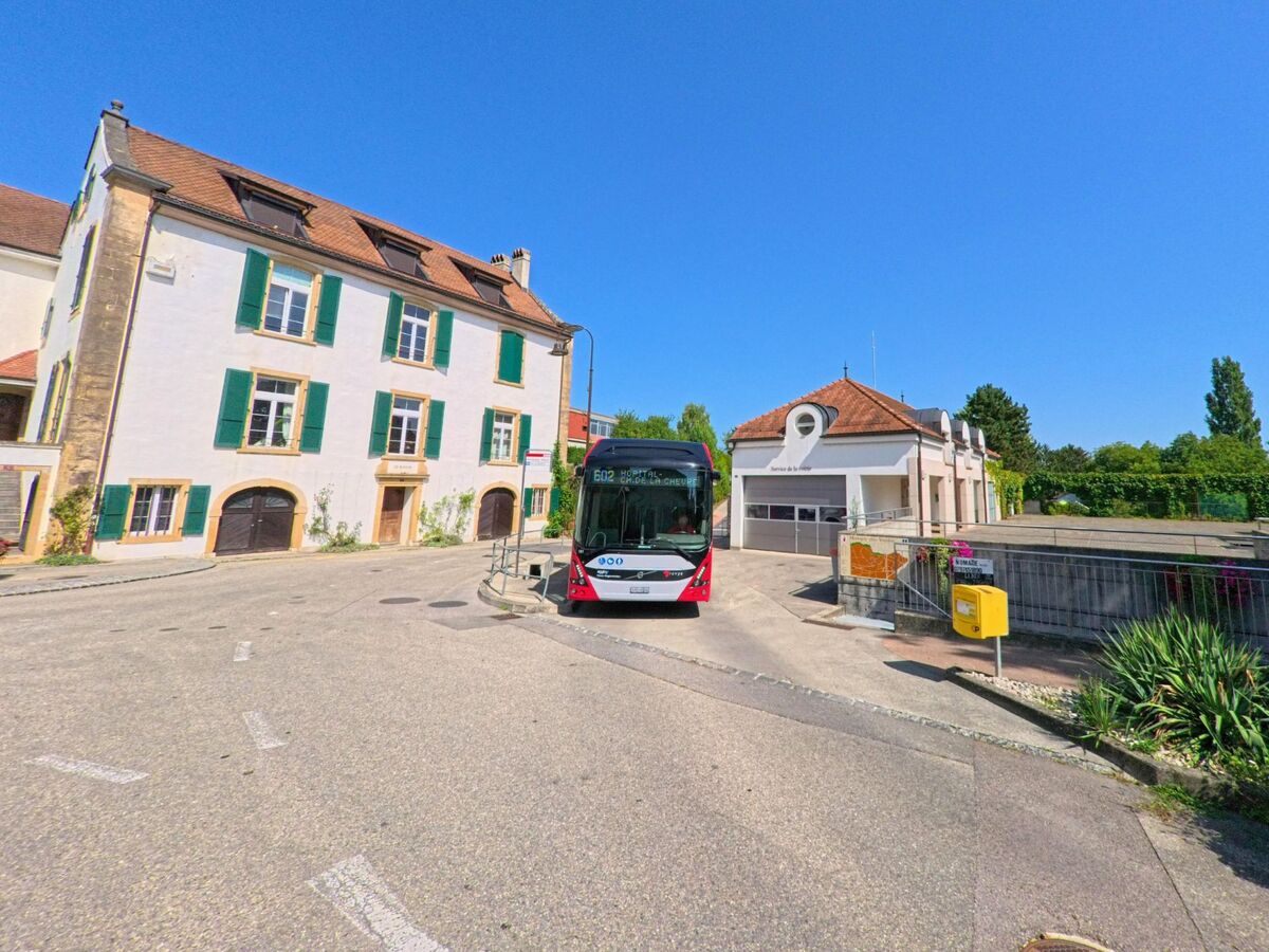 In Montagny-pres-Yverdon (1442, Kanton Waadt) haelt ein roter Linienbus an einer Haltestelle vor traditionellen Wohnhaeusern und einem Gebaeude mit rundem Giebel.