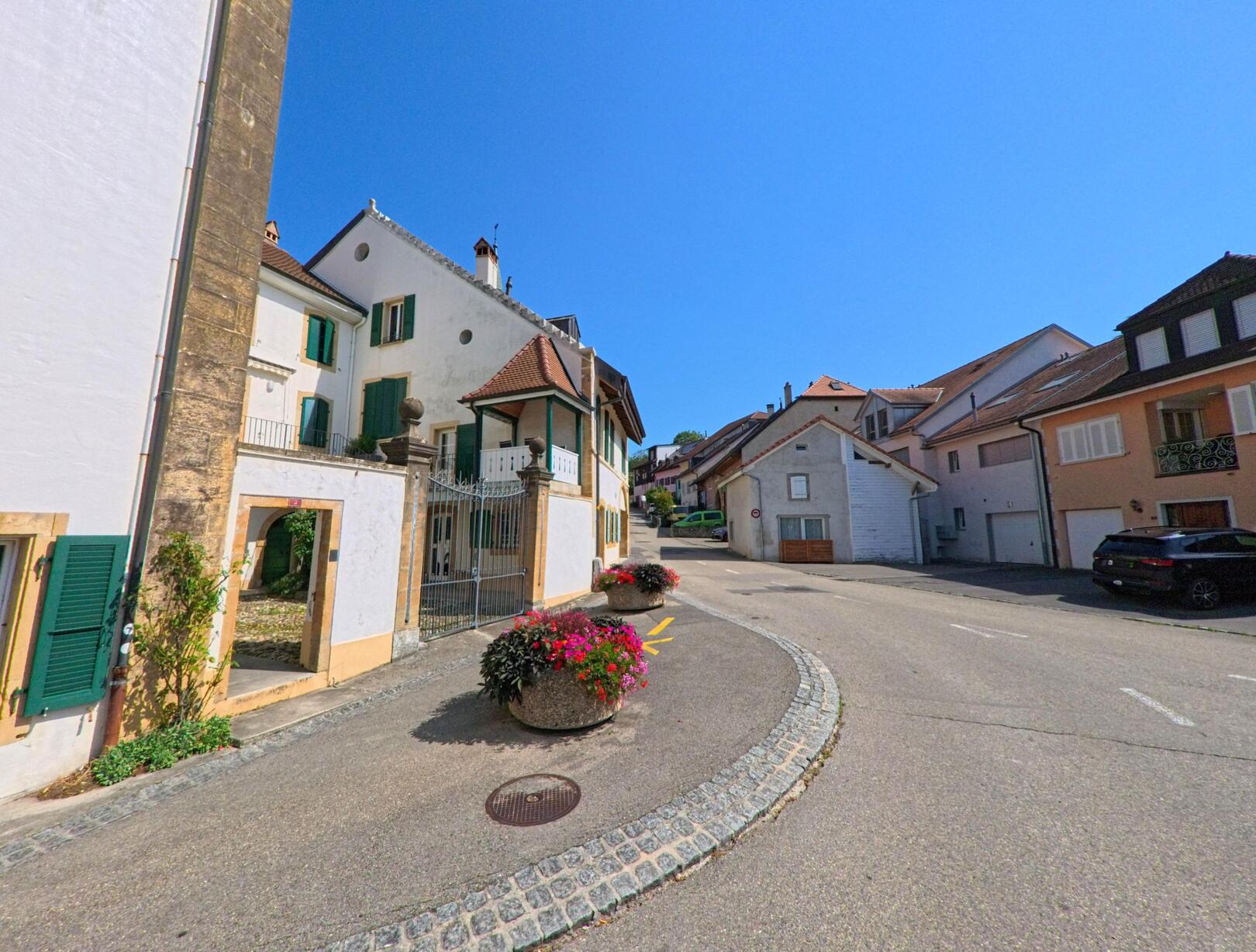 In Montagny-pres-Yverdon (1442, Kanton Waadt) fuehrt eine leicht ansteigende Strasse durch den Dorfkern, gesaeumt von traditionellen Wohnhaeusern mit Fensterlaeden.