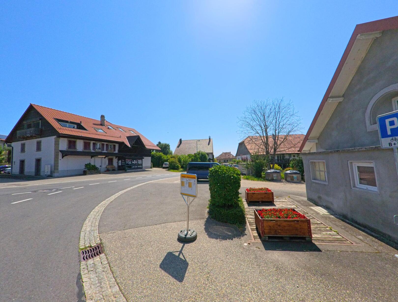 Eine Bushaltestelle mit gelbem Schild steht in Montanaire (1062, Kanton Waadt) an einer Strasse mit Wohnhaeusern und Blumenkuebeln.