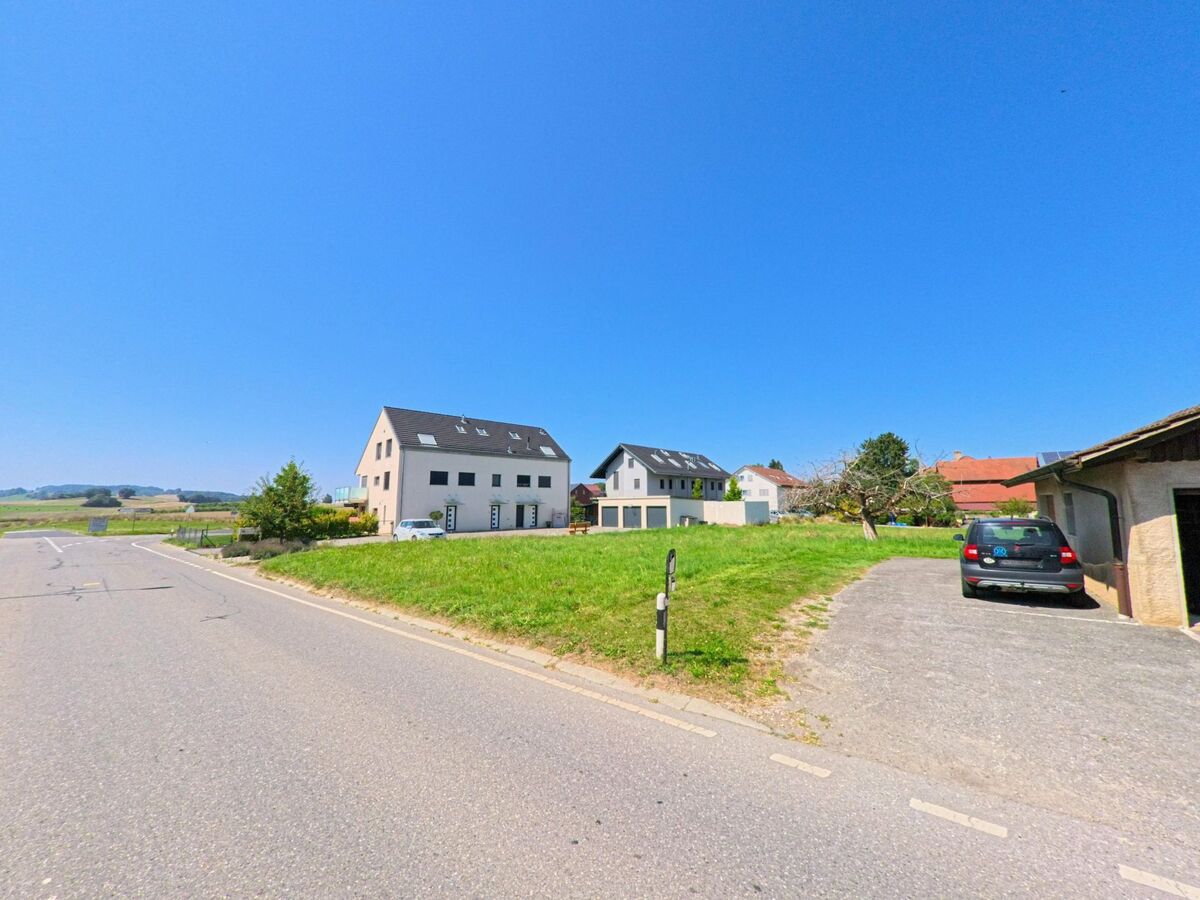 Zwei moderne Mehrfamilienhaeuser mit Solardach stehen in Montanaire (1062, Kanton Waadt) neben einer Strasse mit freier Sicht auf die Felder.