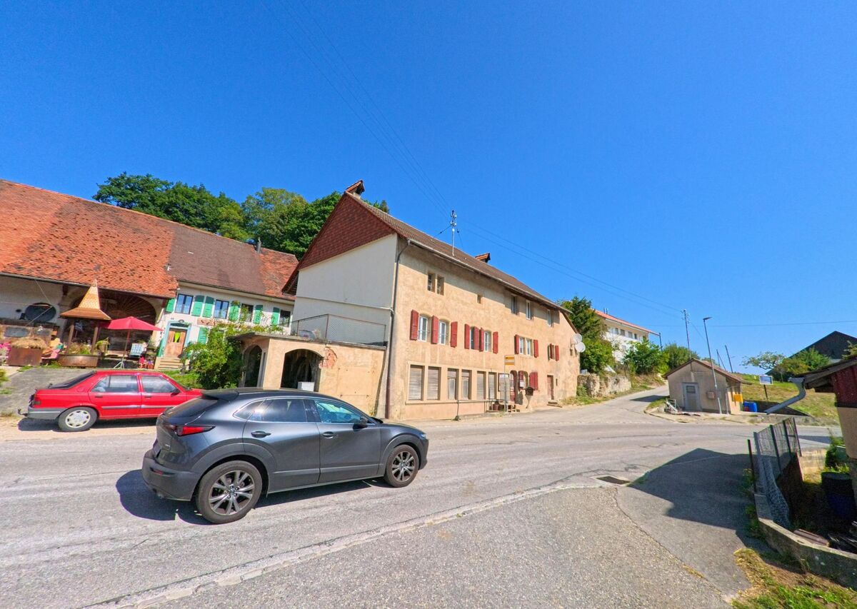 Mehrere traditionelle Wohnhaeuser mit roten Fensterlaeden und Schindeldaechern stehen in Montanaire (1409, Kanton Waadt) entlang einer leicht ansteigenden Strasse.