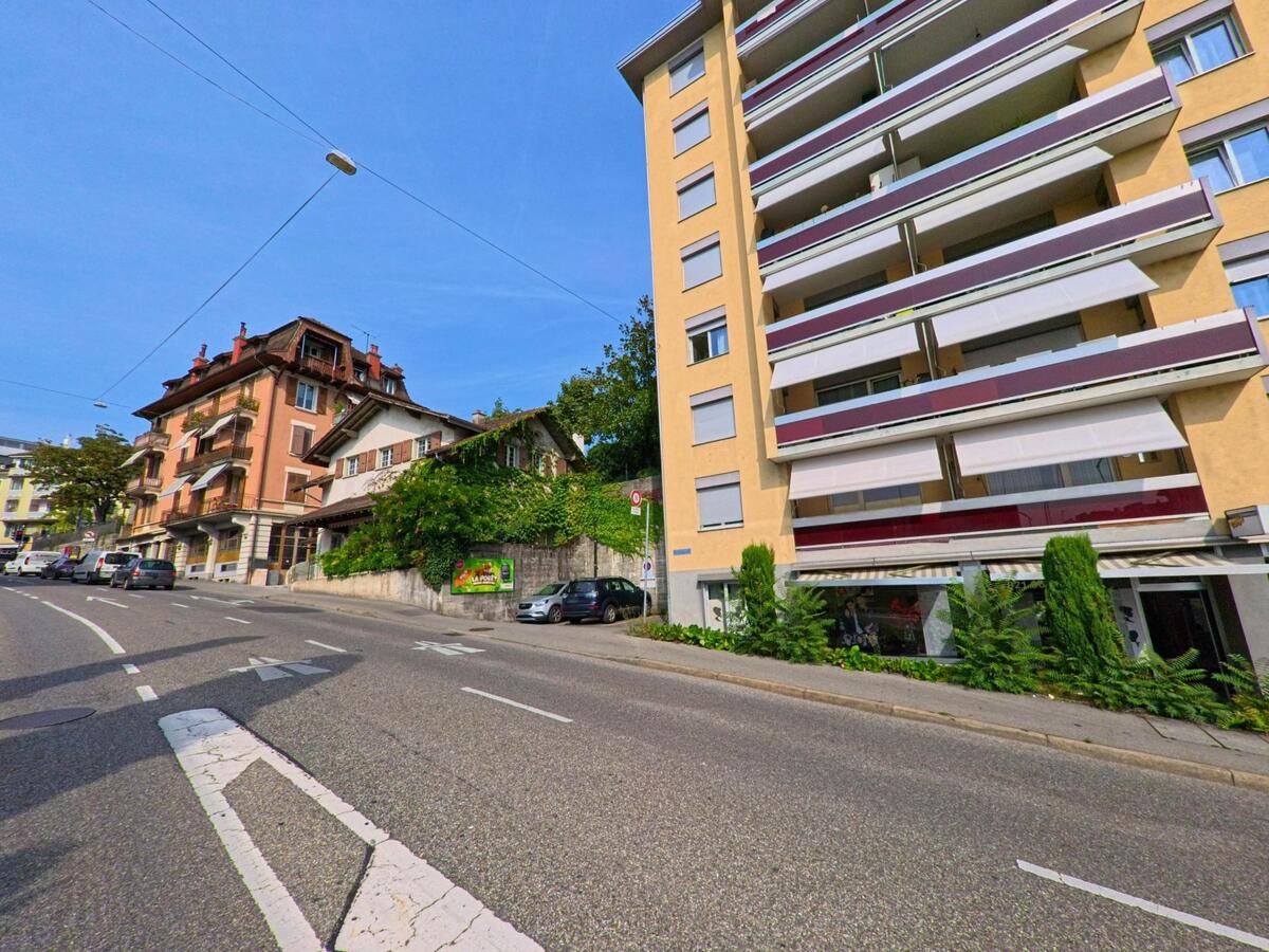 Wohnhaeuser in unterschiedlichen Baustilen saeumen eine ansteigende Strasse in Montreux (1815, Kanton Waadt), wo Autos entlang des Gehwegs parken.