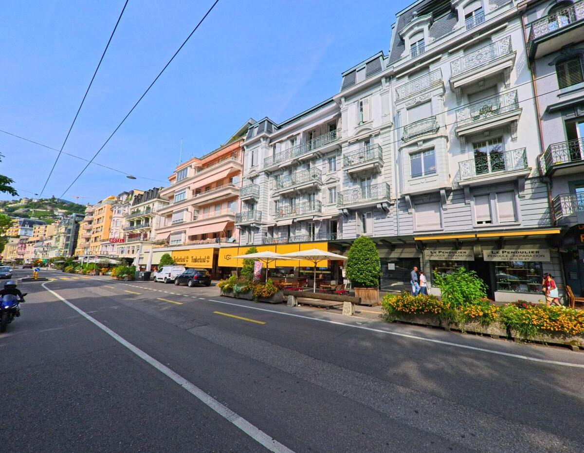 Entlang einer Strasse in Montreux (1822, Kanton Waadt) reihen sich farbenfrohe Wohn- und Geschaeftshauser mit Balkonen und Strassencafes.