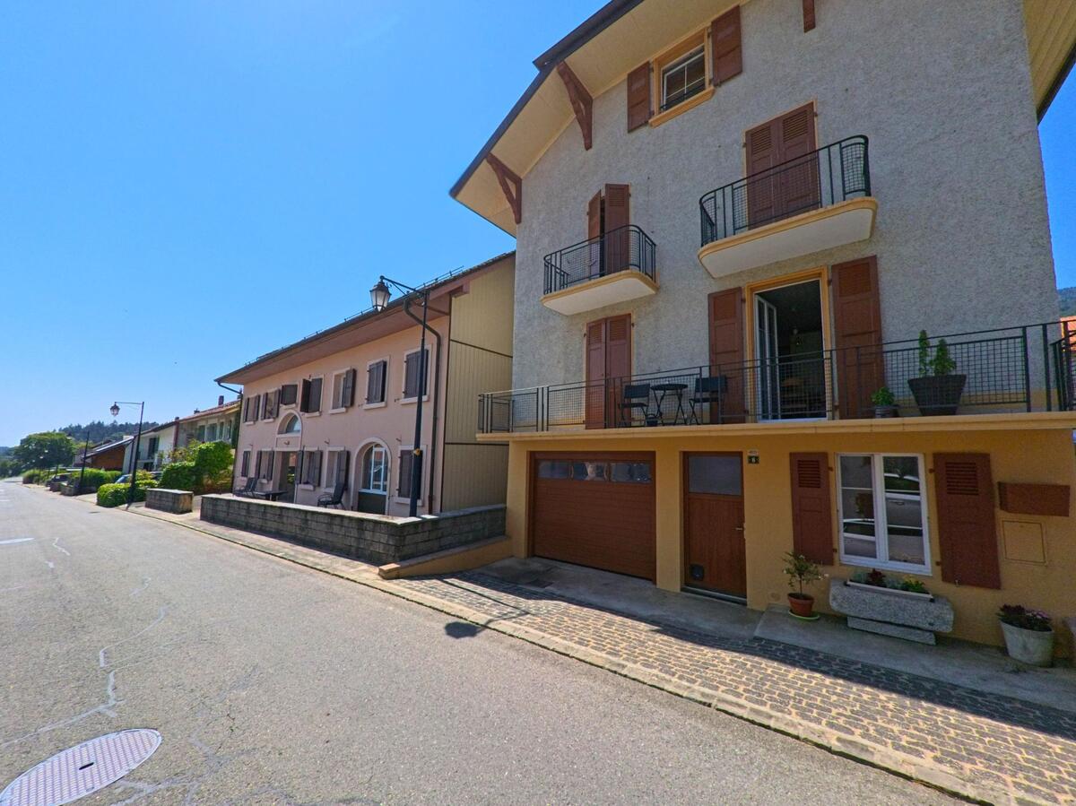 In Montricher (1147, Kanton Waadt) reihen sich Wohnhaeuser mit Balkonen und Holzlaeden entlang einer ruhigen Strasse.