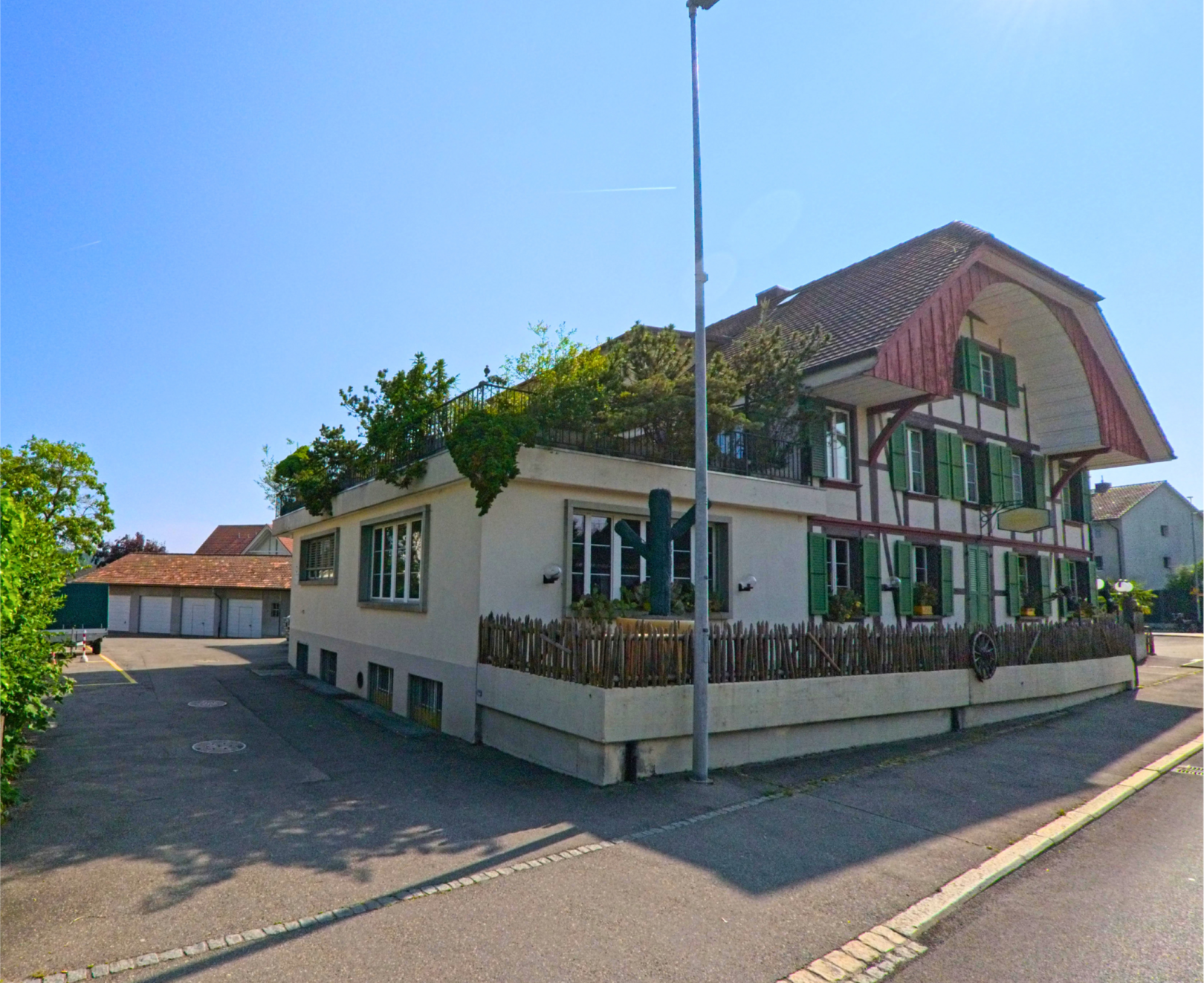 Ein traditionelles Wohnhaus mit grün gestrichenen Fensterläden steht in einer Seitenstrasse von Moosseedorf (3302, Kanton Bern), während die Sonne tief am Himmel scheint.