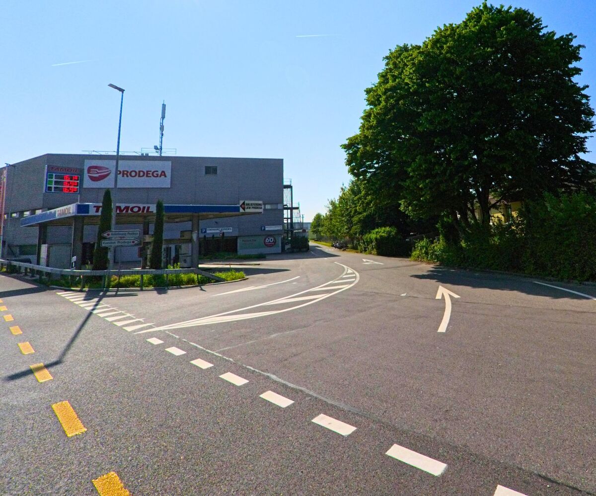 In Moosseedorf (3302, Kanton Bern) liegt eine Tankstelle mit Industriegebäuden am Rand einer verkehrsarmen Kreuzung unter der strahlenden Mittagssonne.