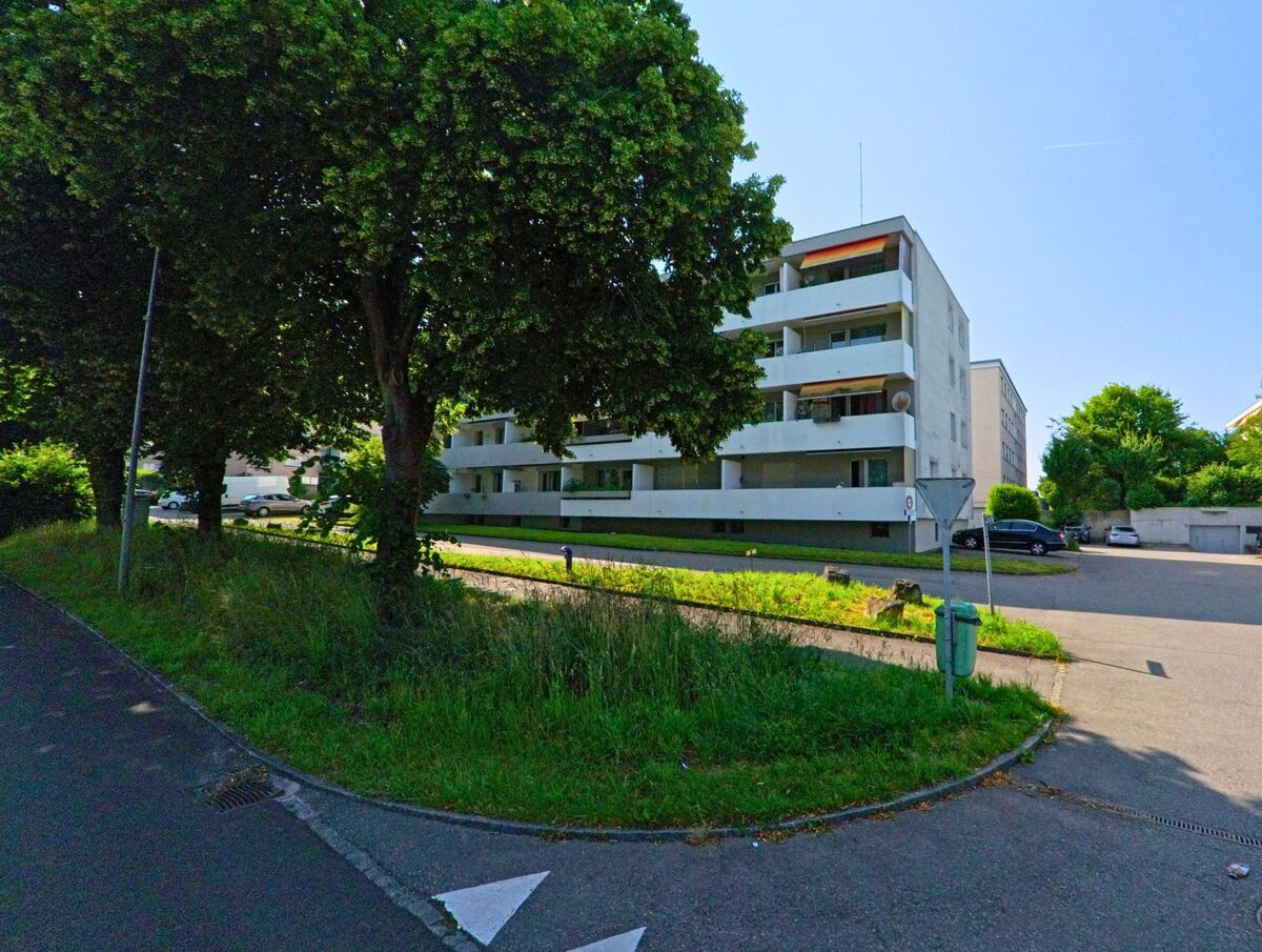 Zwischen mehrstöckigen Wohnhäusern in Moosseedorf (3302, Kanton Bern) liegt ein ruhiger Parkplatz, gesäumt von Bäumen und gepflegtem Grün.