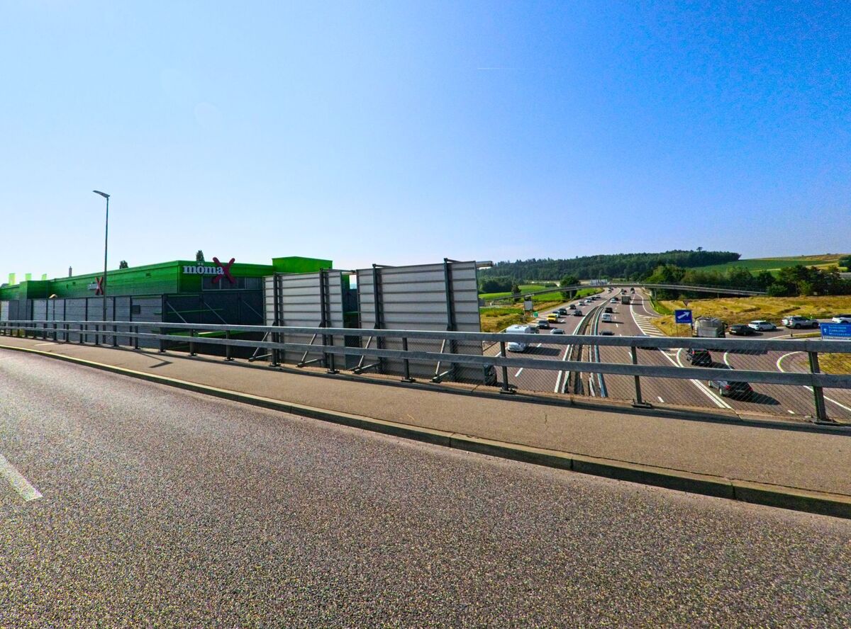 Auf einer Brücke über der Autobahn bei Moosseedorf (3321, Kanton Bern) ist der Blick frei auf den dichten Verkehr und ein auffällig grünes Gewerbegebäude am Strassenrand.