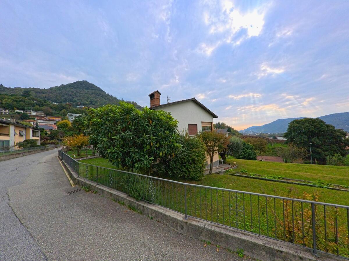 Ein Einfamilienhaus mit Garten liegt an einer ruhigen Strasse in Morbio Inferiore (6834, Kanton Tessin) mit Blick auf die bewaldeten Hügel der Umgebung.