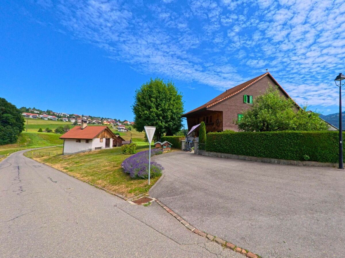 In Morlon (1638, Kanton Freiburg) steht ein traditionelles Bauernhaus mit grünen Fensterläden an einer kleinen Kreuzung, umgeben von Lavendel und gepflegtem Garten.
