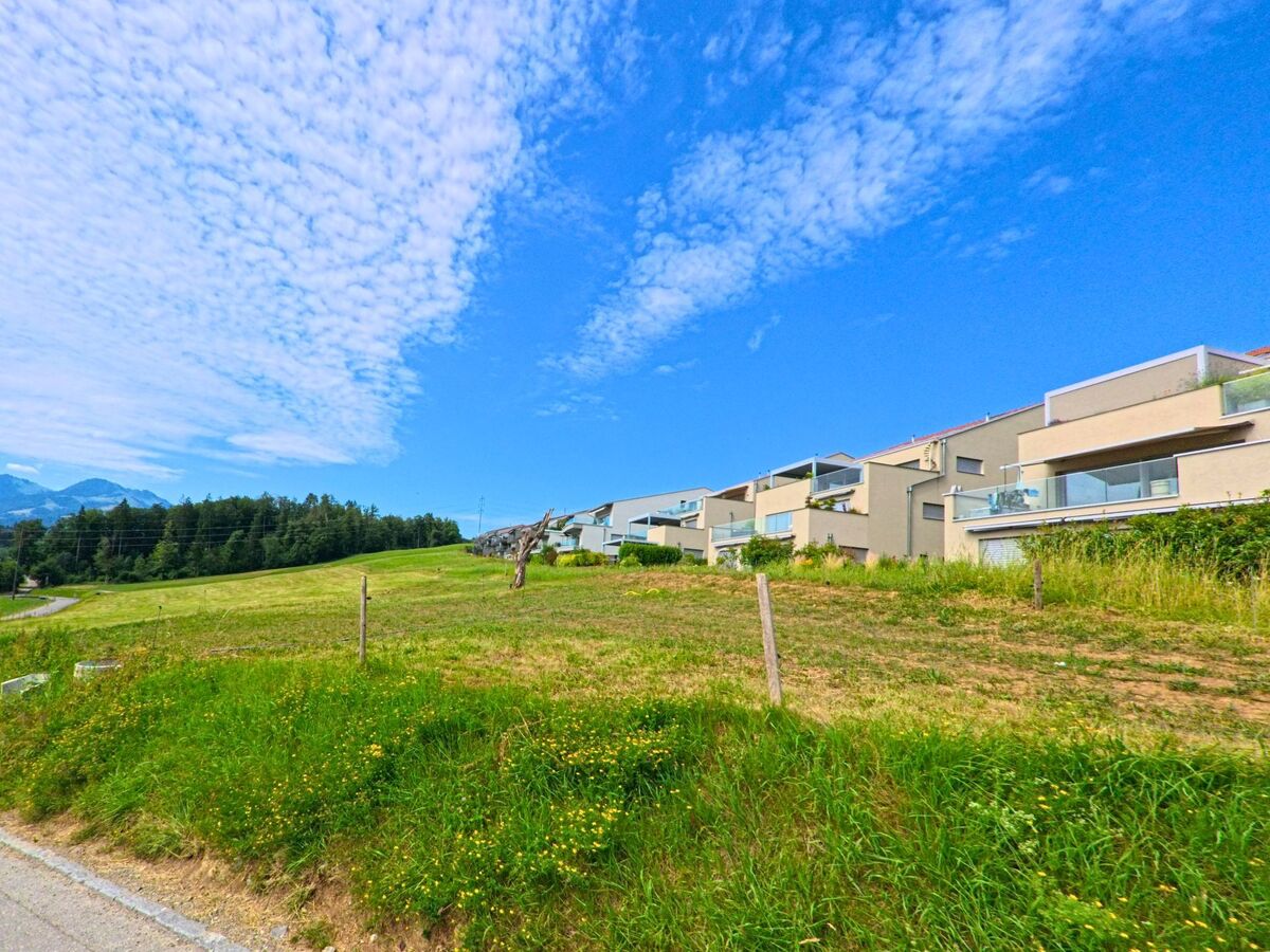 In Morlon (1638, Kanton Freiburg) grenzen moderne Terrassenwohnungen direkt an eine offene Wiese, hinter der sich ein Wald und die Berge abzeichnen.