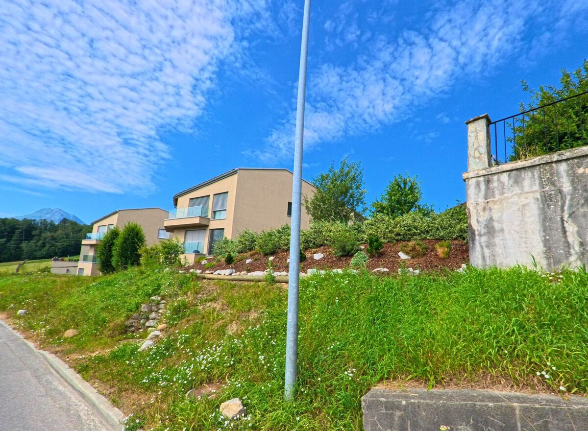 Am Hang von Morlon (1638, Kanton Freiburg) stehen moderne Wohnhäuser mit Balkonen, eingefasst von gepflegten Gärten und einer Natursteinmauer.