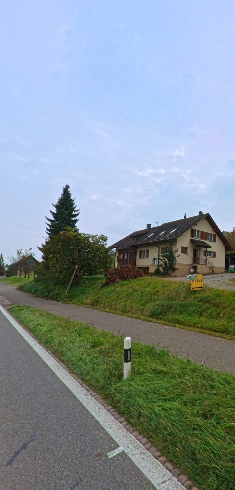 Am Ortsrand von Mühlau (5642, Kanton Aargau) steht ein Einfamilienhaus mit Obstverkaufsschild, umgeben von Grünflächen und einem Fussweg entlang der Strasse.