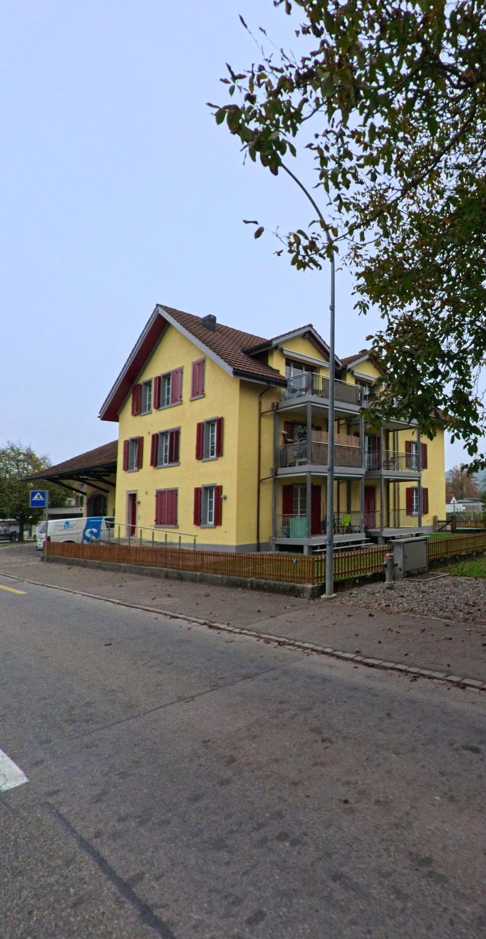 Ein gelbes Mehrfamilienhaus mit roten Fensterläden steht an der Hauptstrasse in Mülligen (5243, Kanton Aargau) und verfügt über Balkone auf mehreren Etagen.