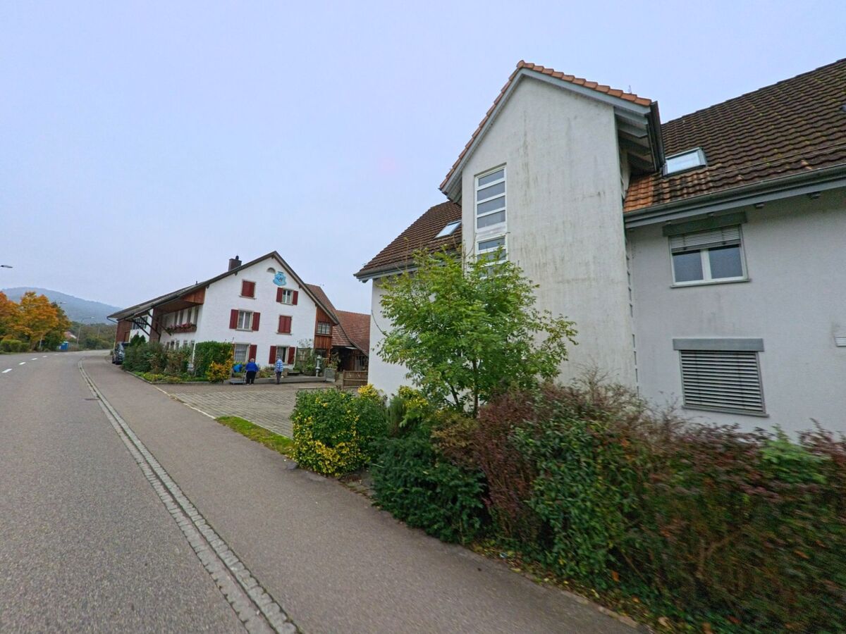 Entlang der Hauptstrasse in Mülligen (5243, Kanton Aargau) stehen traditionelle Wohnhäuser mit gepflegten Vorgärten und Blick auf die herbstliche Landschaft.