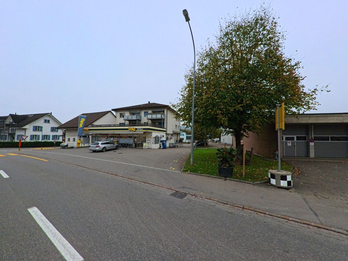 An der Hauptstrasse von Mülligen (5243, Kanton Aargau) befindet sich ein Volg-Laden mit Parkplätzen und angrenzenden Wohnhäusern in zentraler Dorflage.