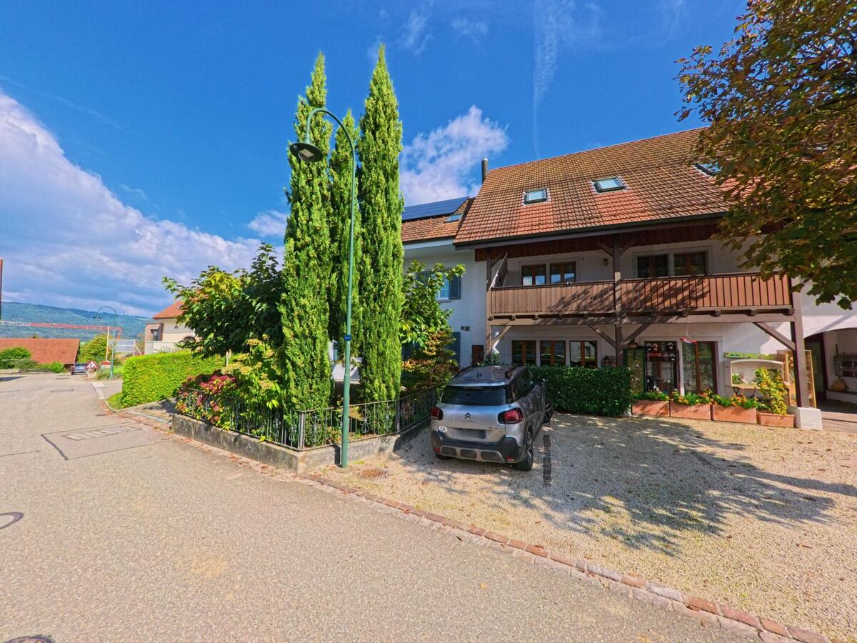 Ein Wohnhaus mit Holzbalkon und hohen Zypressen steht an einer sonnigen Strasse in Münchwilen (4333, Kanton Aargau).